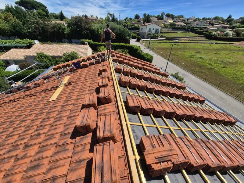 Tuiles de Marseille vieillies réparties en piles sur le toit, pose en cours sur le premier versant