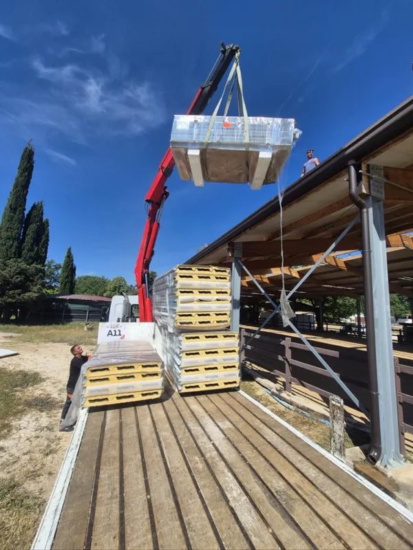 Grue de camion hissant un paquet de panneaux sandwich isolés sur la toiture d'une écurie